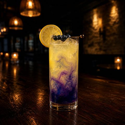 The Bluebonnet Byway: a tall lemon cocktail with a blue-violet blueberry swirl, lemon wheel, and blueberries on a pick