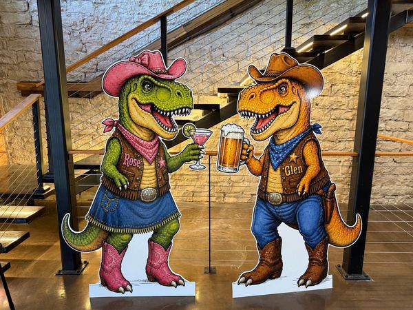 Glen and Rose, the Palace's two cowboy T-rex mascots, toasting in front of the limestone wall