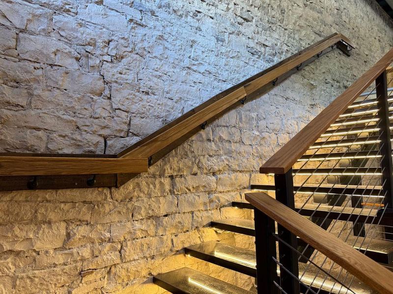 Oak handrail and LED-lit floating stairs mounted on the original rough limestone wall